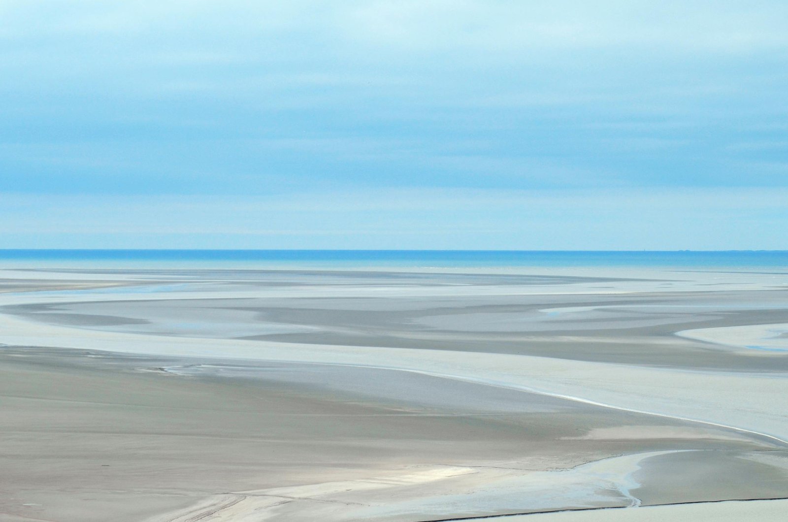 Peaceful beach view showcasing expansive sandbars and calm ocean under a cloudy sky.